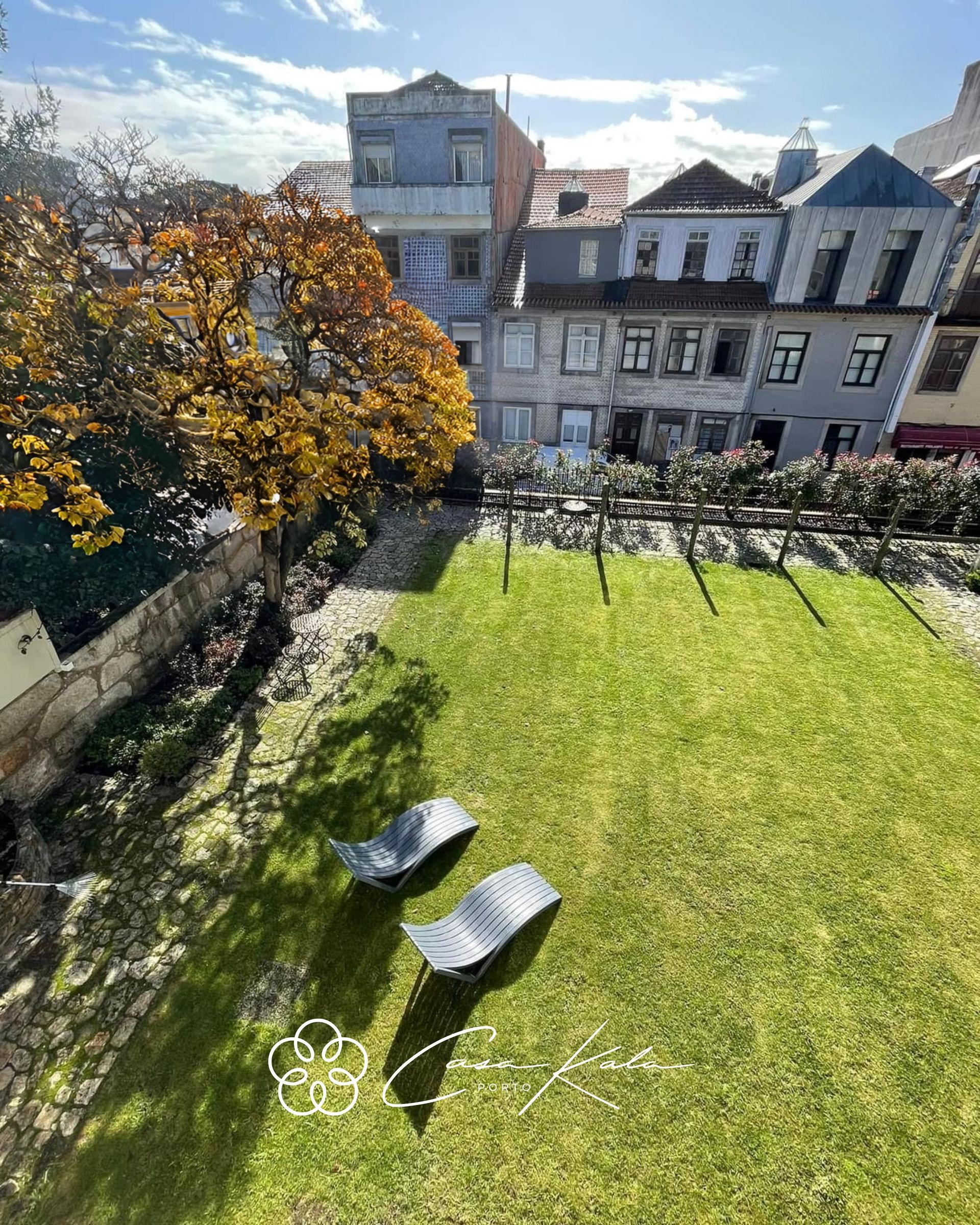 Sunlit garden at Casa Kala Porto, with lounge chairs and city backdrop in autumn.