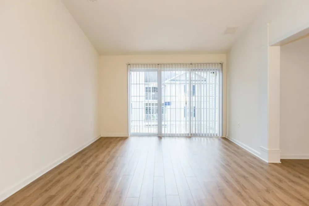 An empty living room with hardwood floors and sliding glass doors.