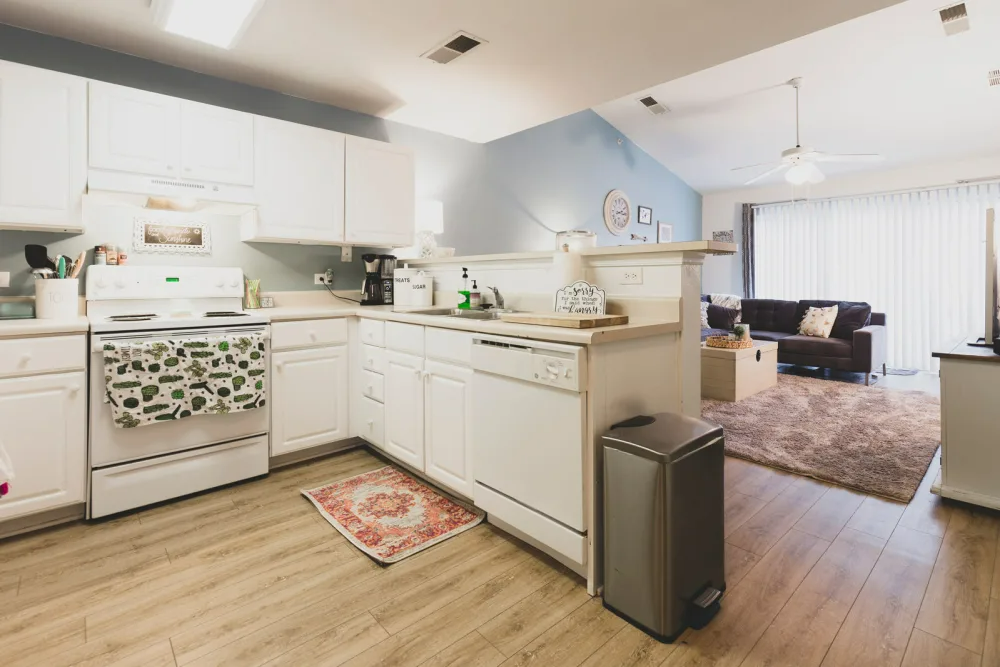 A kitchen with white cabinets, a stove, a dishwasher, and a trash can.