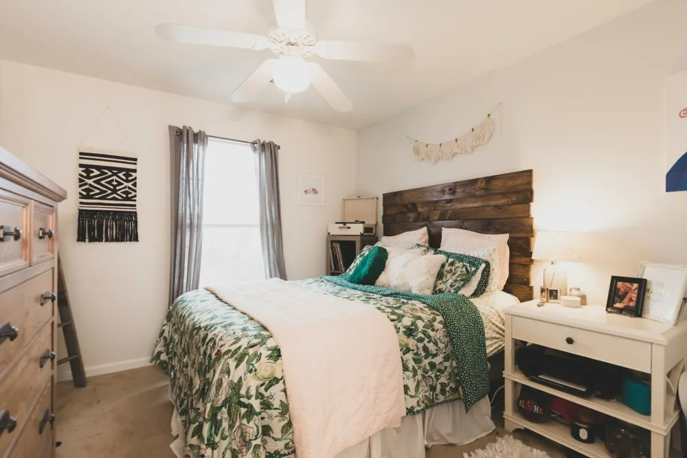 A bedroom with a bed, dresser, nightstand, and ceiling fan.