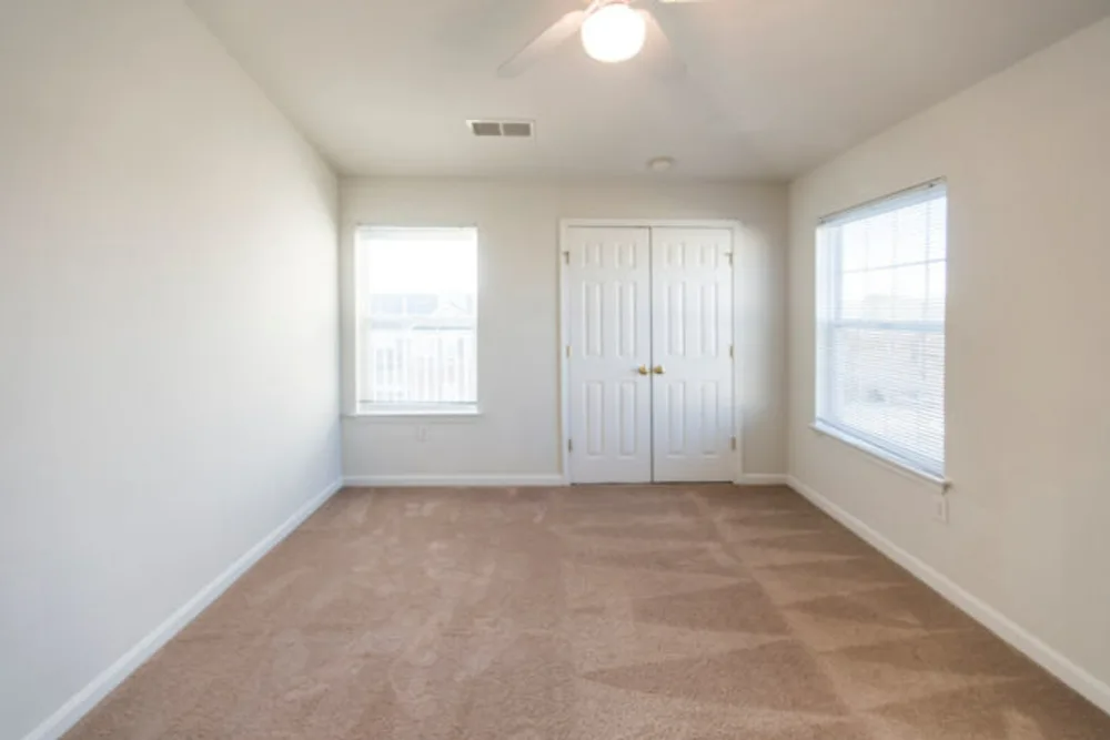 An empty bedroom with two windows and a ceiling fan.