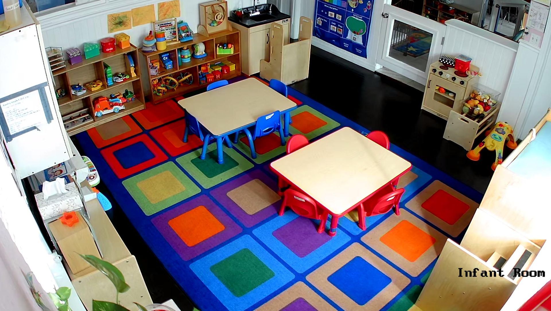 An infant room with tables and chairs and a colorful rug