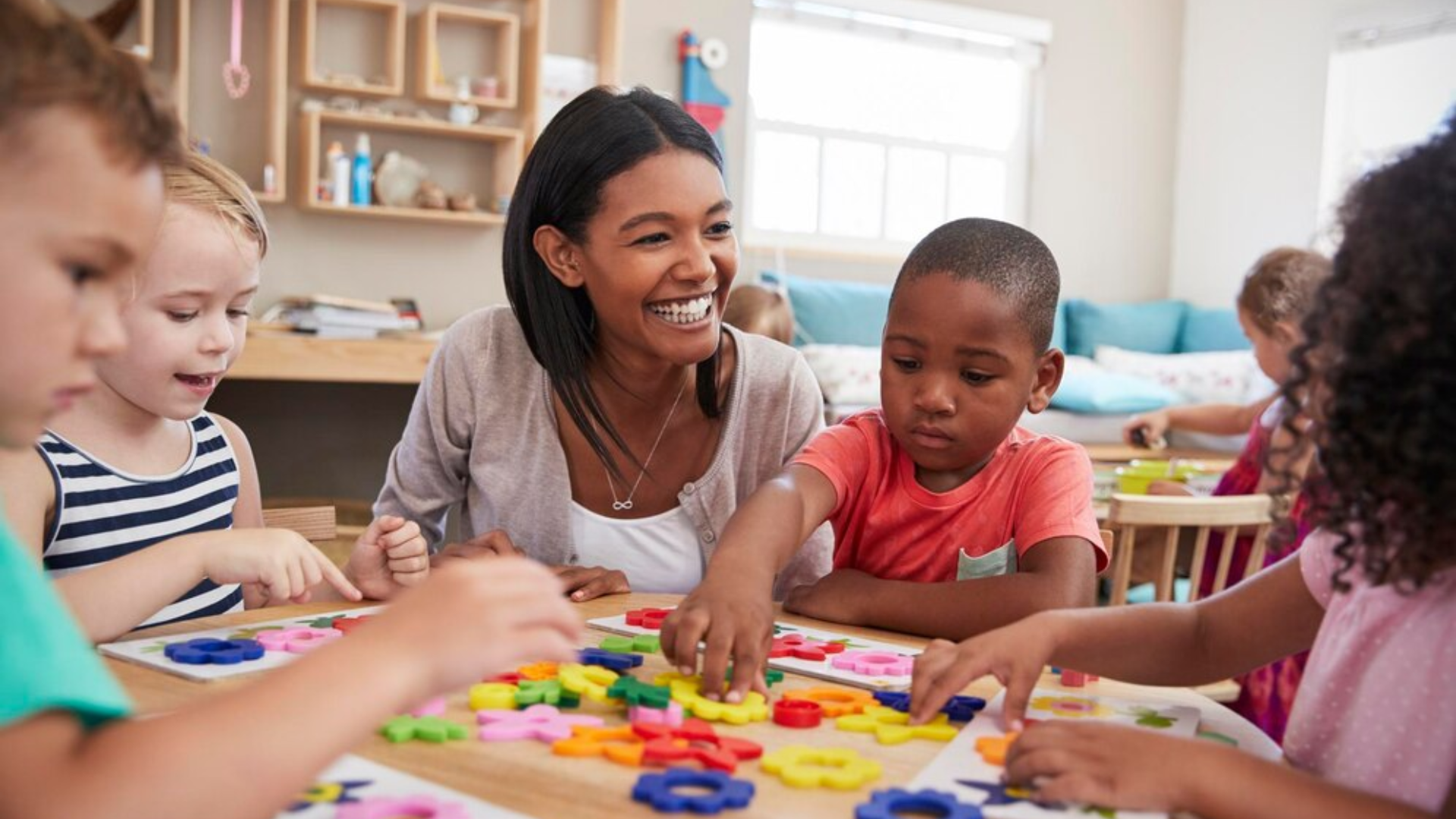 A teacher is playing with a group of children at a table in a classroom.