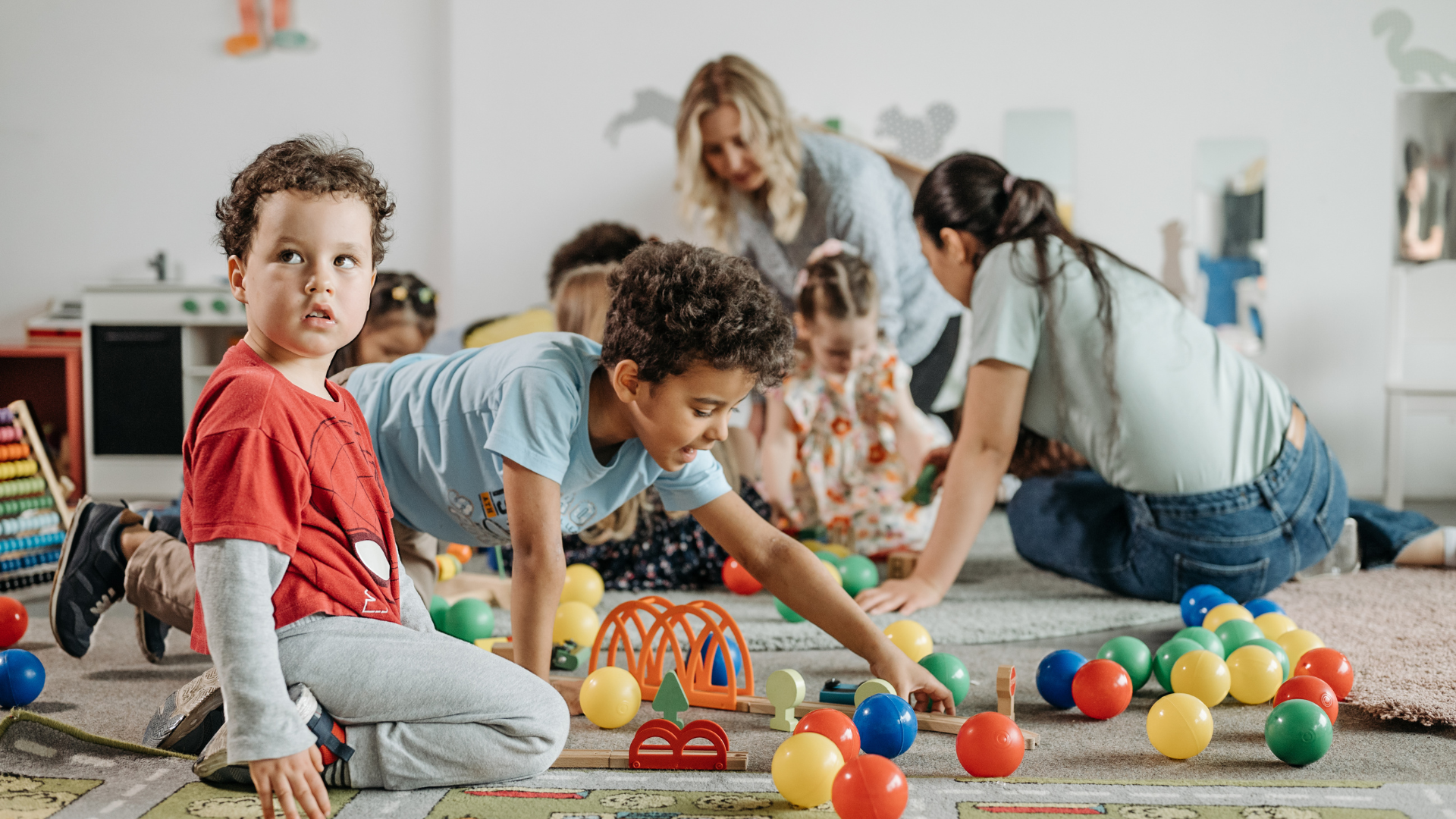A group of children are playing with balls on the floor in a classroom.