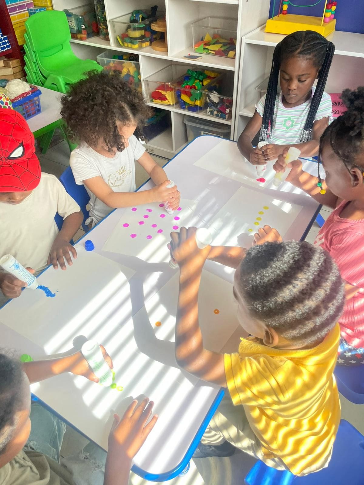 Preschoolers crafting at a table in bright Raising Angels classroom.