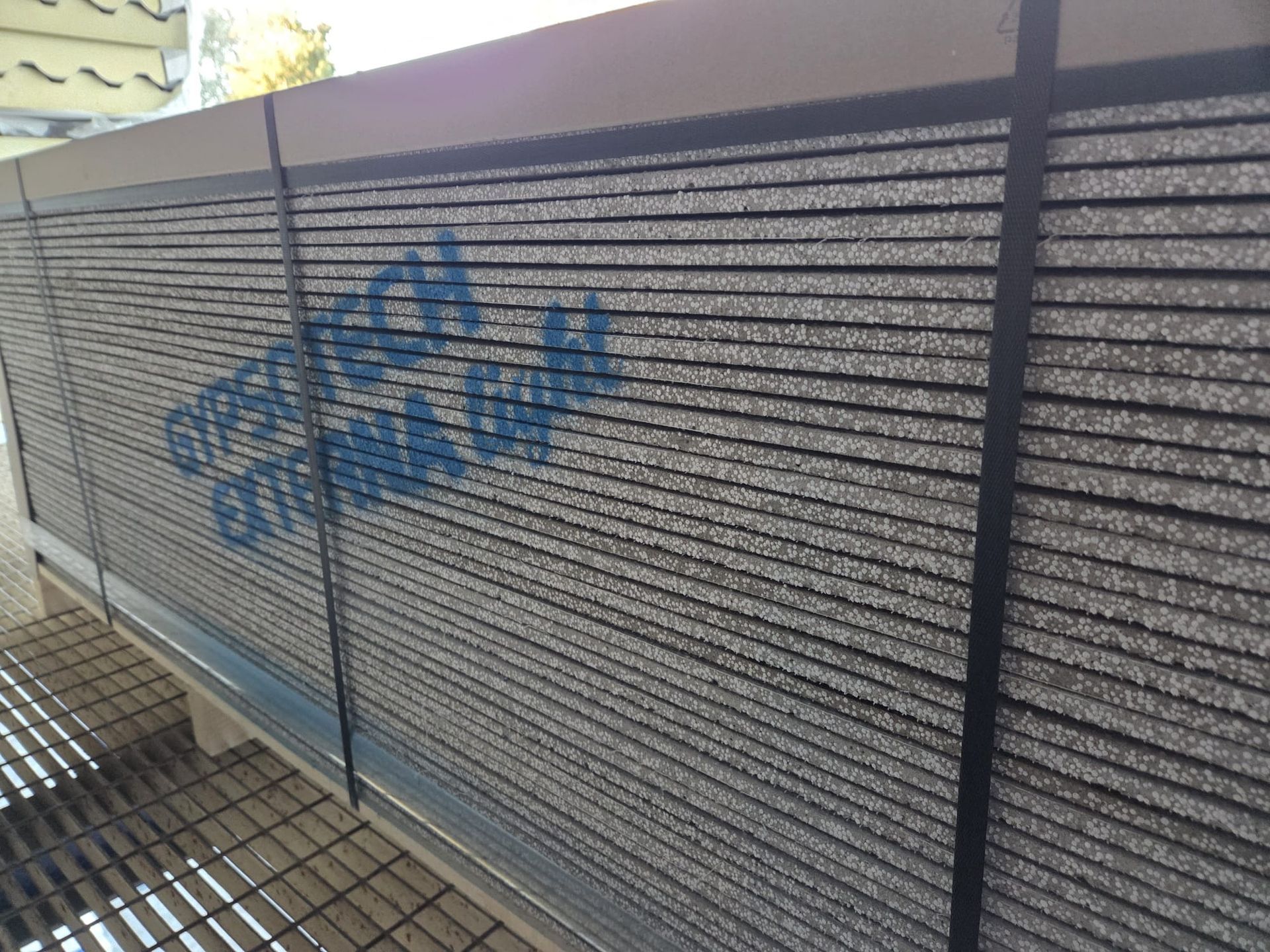 Insieme di pannelli da costruzione grigi fissati con cinghie nere su un telaio metallico. Testo blu visibile.