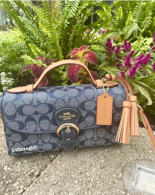 A coach purse is sitting on a sidewalk next to flowers.
