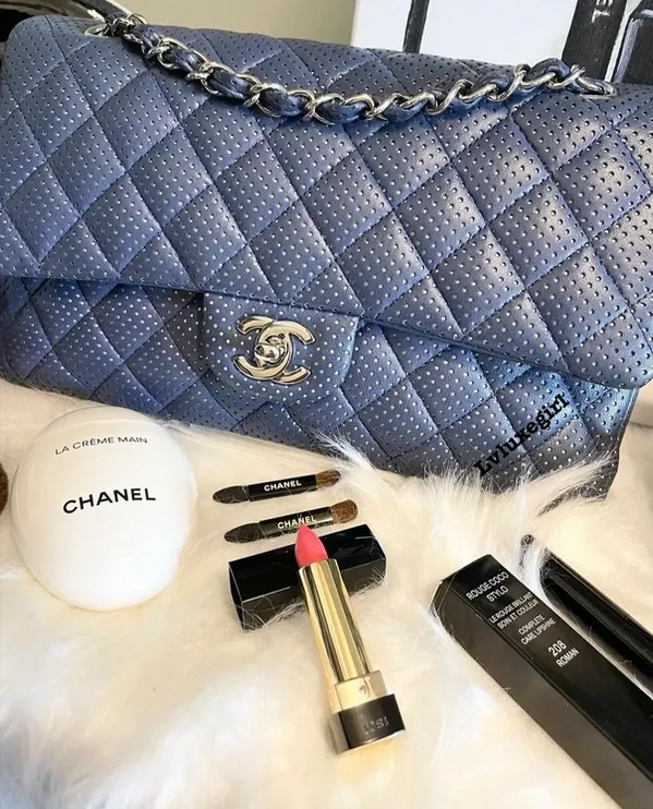 A blue chanel purse is sitting on top of a white fur blanket.