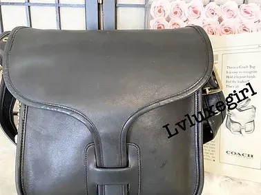 A black leather messenger bag is sitting on a table next to a book.