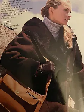A woman in a brown coat is holding a purse that says luluxgirl