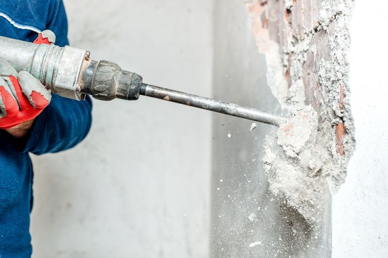 Person using a power drill to break apart a concrete wall.