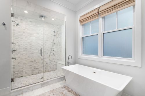 Modern bathroom with a white freestanding tub, glass shower, and window with shades.