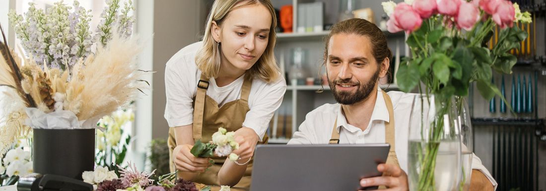 A female and male florist at a store counter looking at a computer.