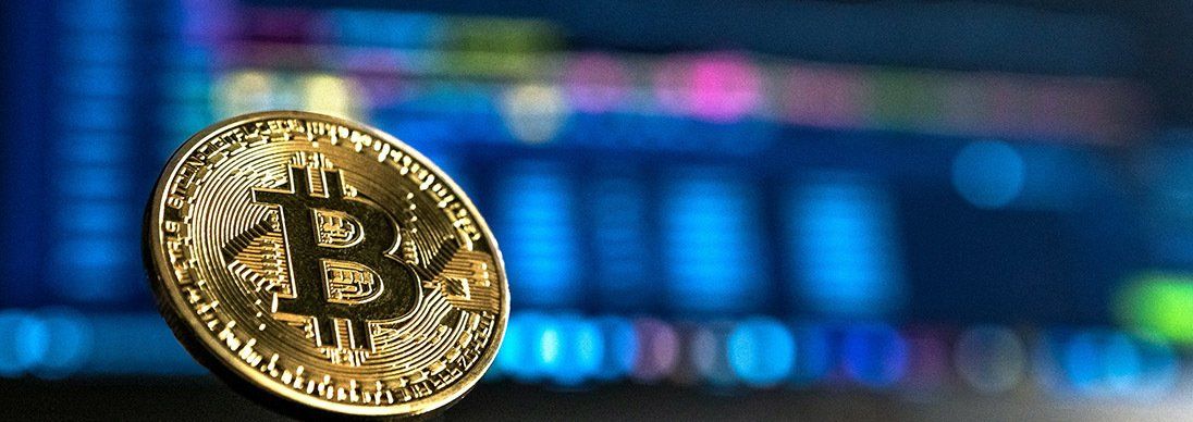 Image of single gold bitcoin with blurred computer screen in the background