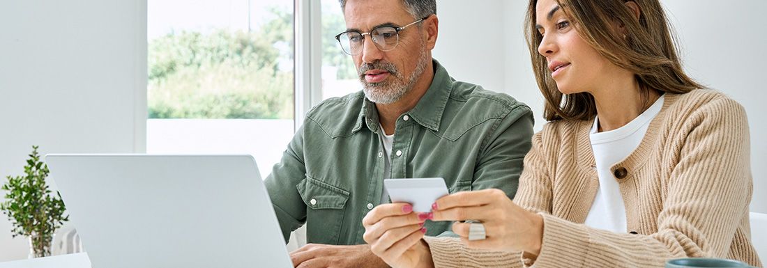 A man and a woman looking at a computer and holding a credit card as if to be making a payment