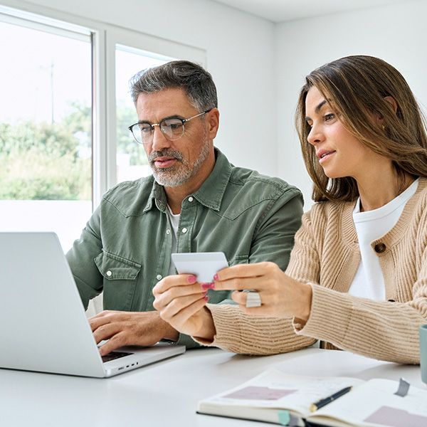 Man and woman looking at a computer and holding a credit card as if to be making a payment
