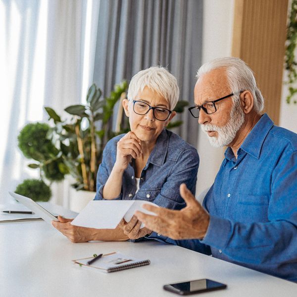A woman with grey hair and man with grey hair and a beard seated at a table looking at paperwork