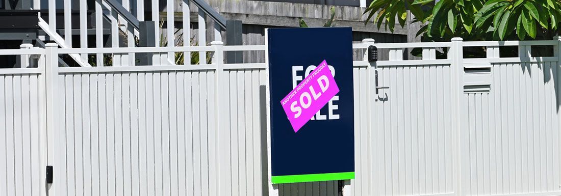 A sold sign outside of a home with a white fence