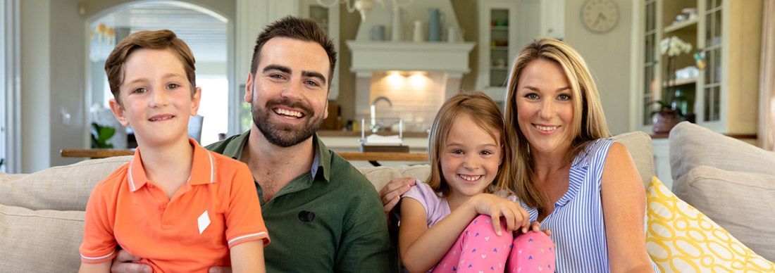 Family of four in their lounge room smiling and looking at the camera