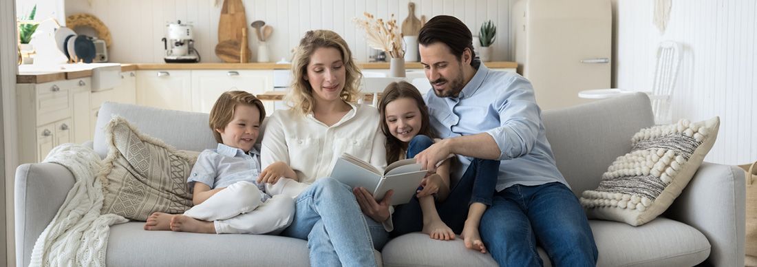 Parents sitting on a sofa with two children. They are reading together.