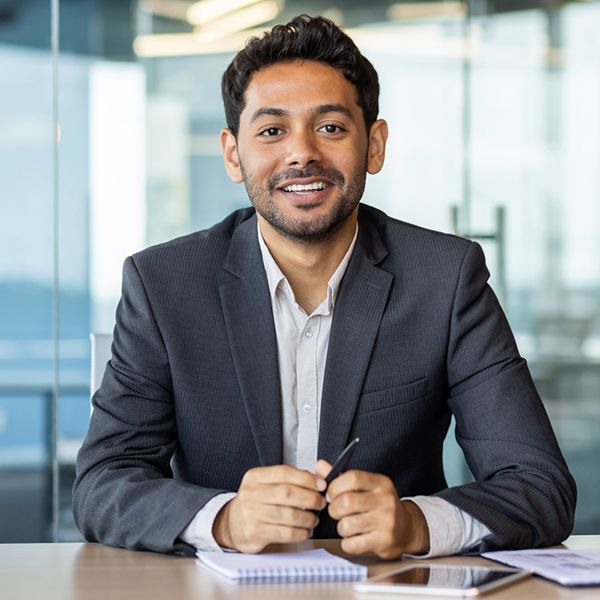 Young hispanic man dressed in a suit sitting at a desk.
