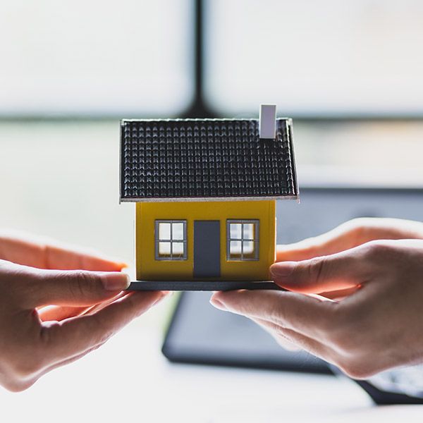 Two hands with a model of a home between them as if to be transferring ownership