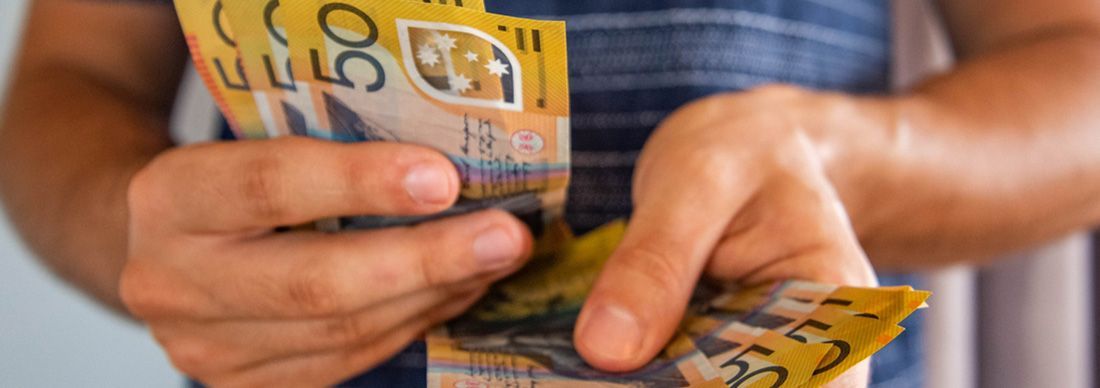 Young man counting $50 notes in Australian currency, indicative of the federal budget 2024-25