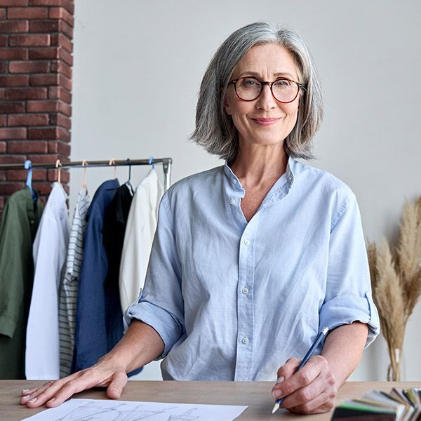 Woman business owner with grey hair and a blue shirt at a bench, looking at the camera.