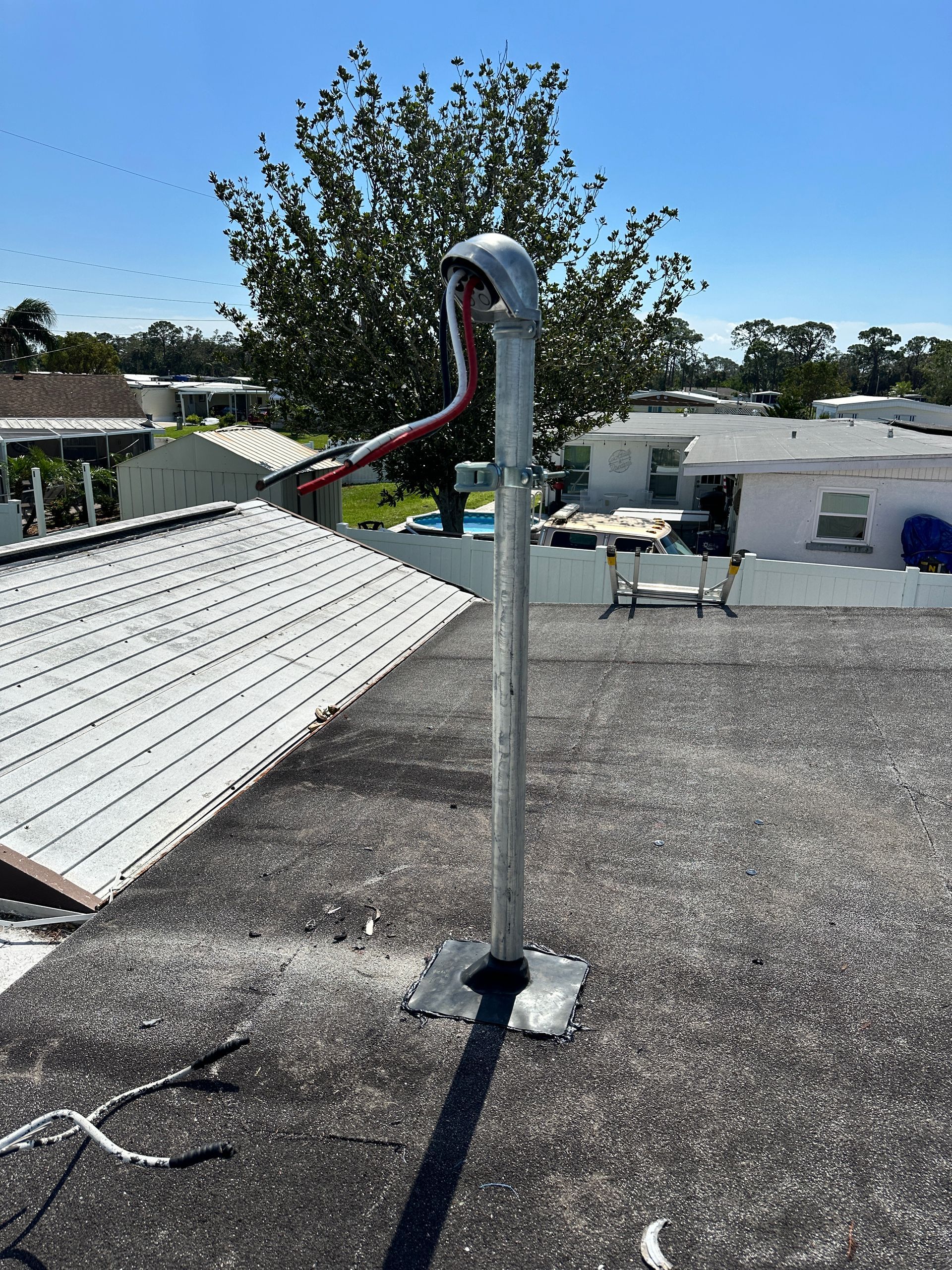 A metal pipe on a flat roof with a bent top and a red hose, under a blue sky.