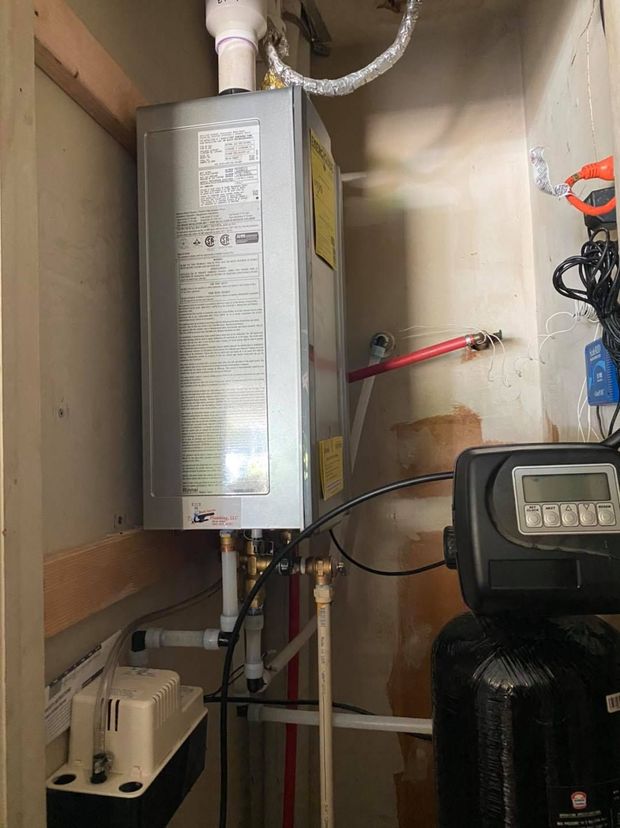 A water heater is sitting in a closet next to a water softener.
