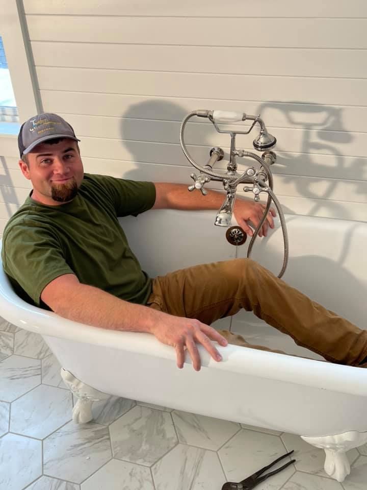 A man is sitting in a bathtub holding a faucet.