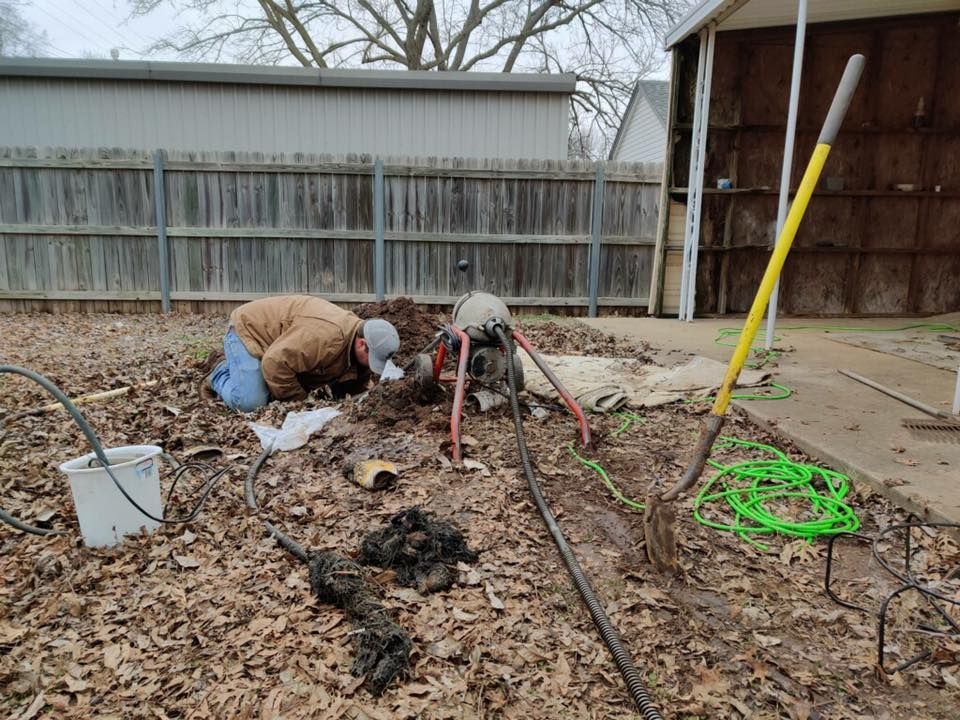 A man is kneeling down in the dirt in front of a fence.