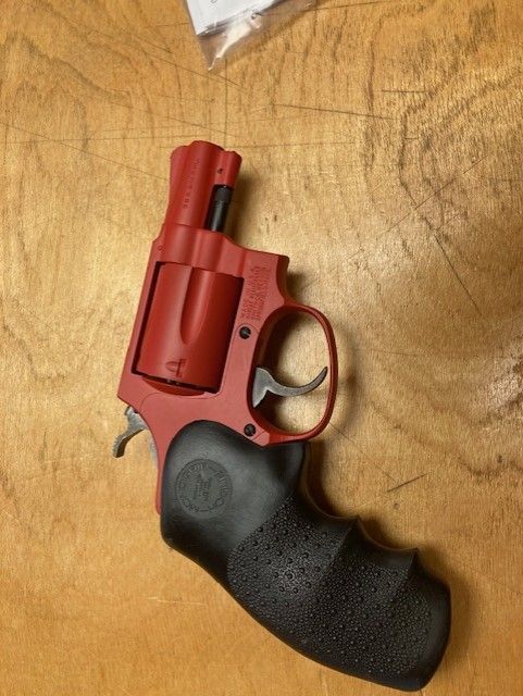 A red revolver is sitting on a wooden table.