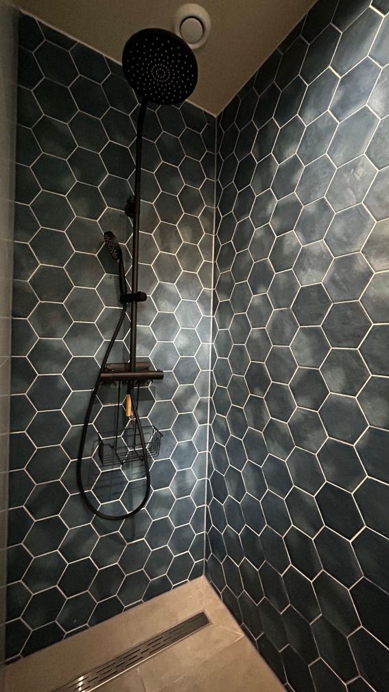 Een douche met zwarte tegels en een zwarte douchekop. Vakantiewoning Boshuisje de Leeuwerik