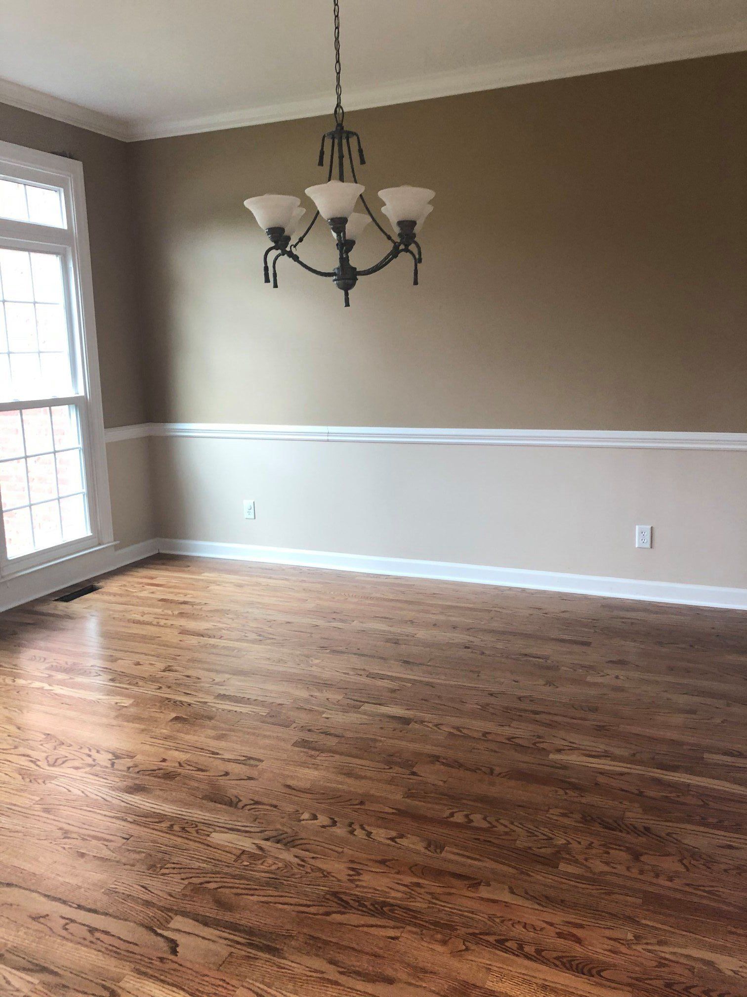 An empty dining room with hardwood floors and a chandelier hanging from the ceiling.