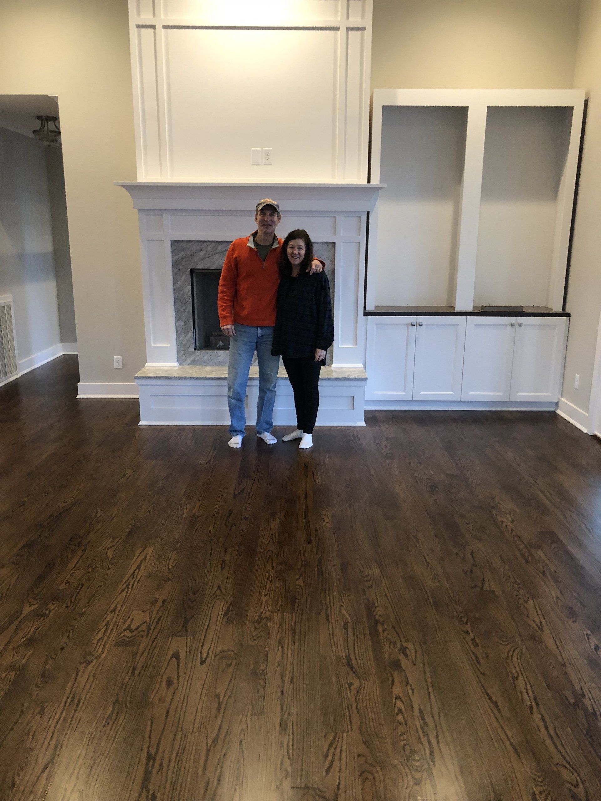 A man and a woman are standing in front of a fireplace in a living room.