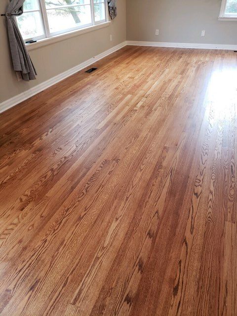 A living room with hardwood floors and two windows.