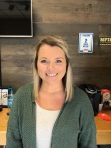 A woman in a green sweater is smiling in front of a wooden wall.