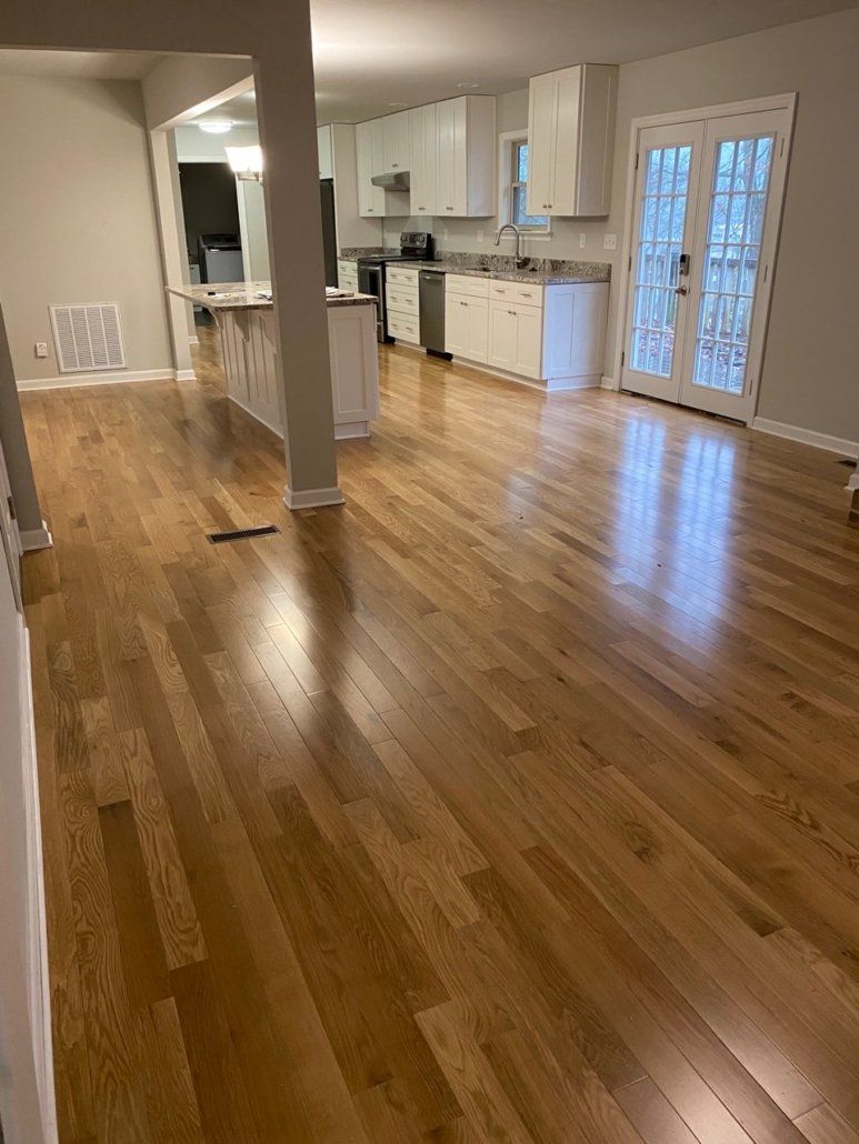 A living room with hardwood floors and a kitchen in the background.