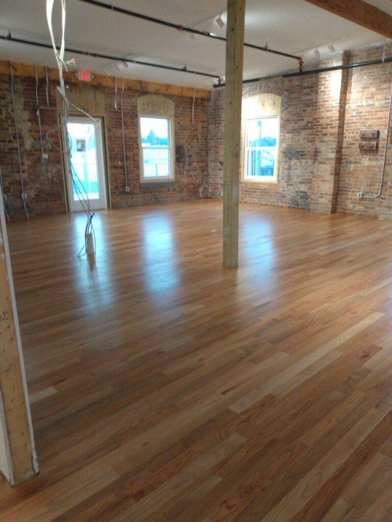 A large empty room with wooden floors and brick walls.