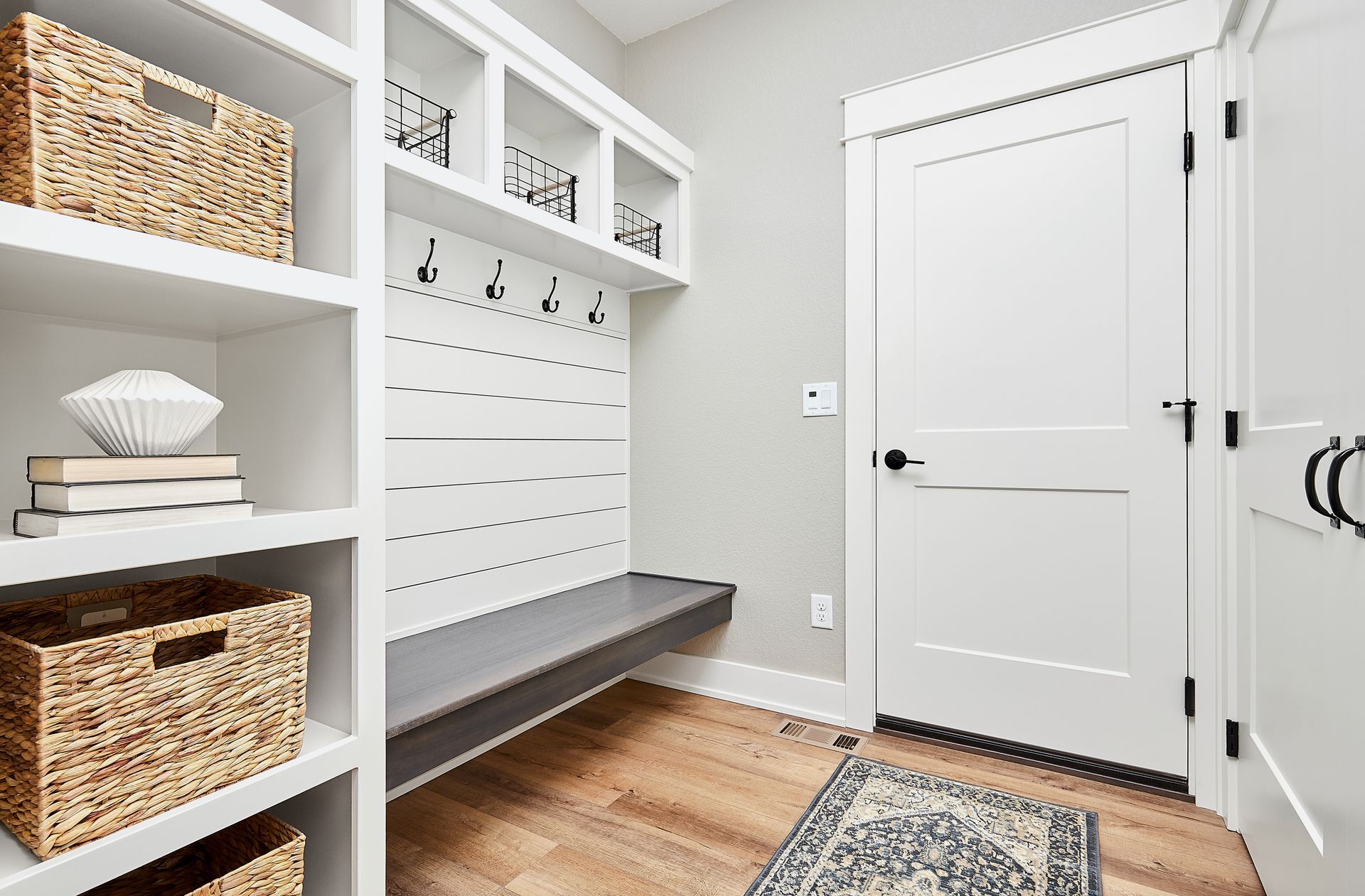A mud room with a bench , shelves , hooks and a rug.