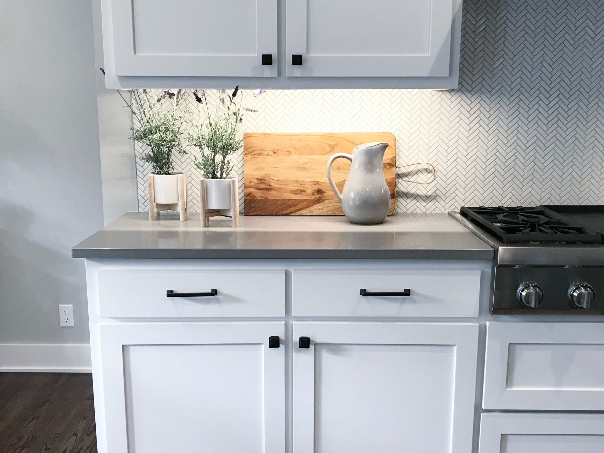 A kitchen with white cabinets , a stove , and a pitcher on the counter.