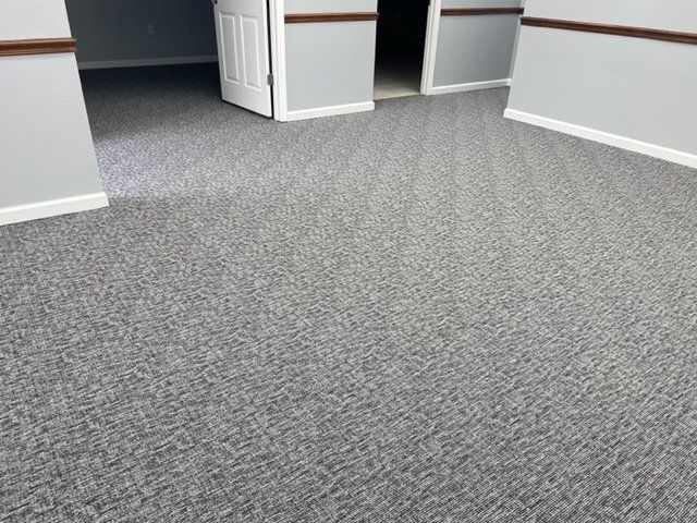 A room with a gray carpeted floor and two doors.