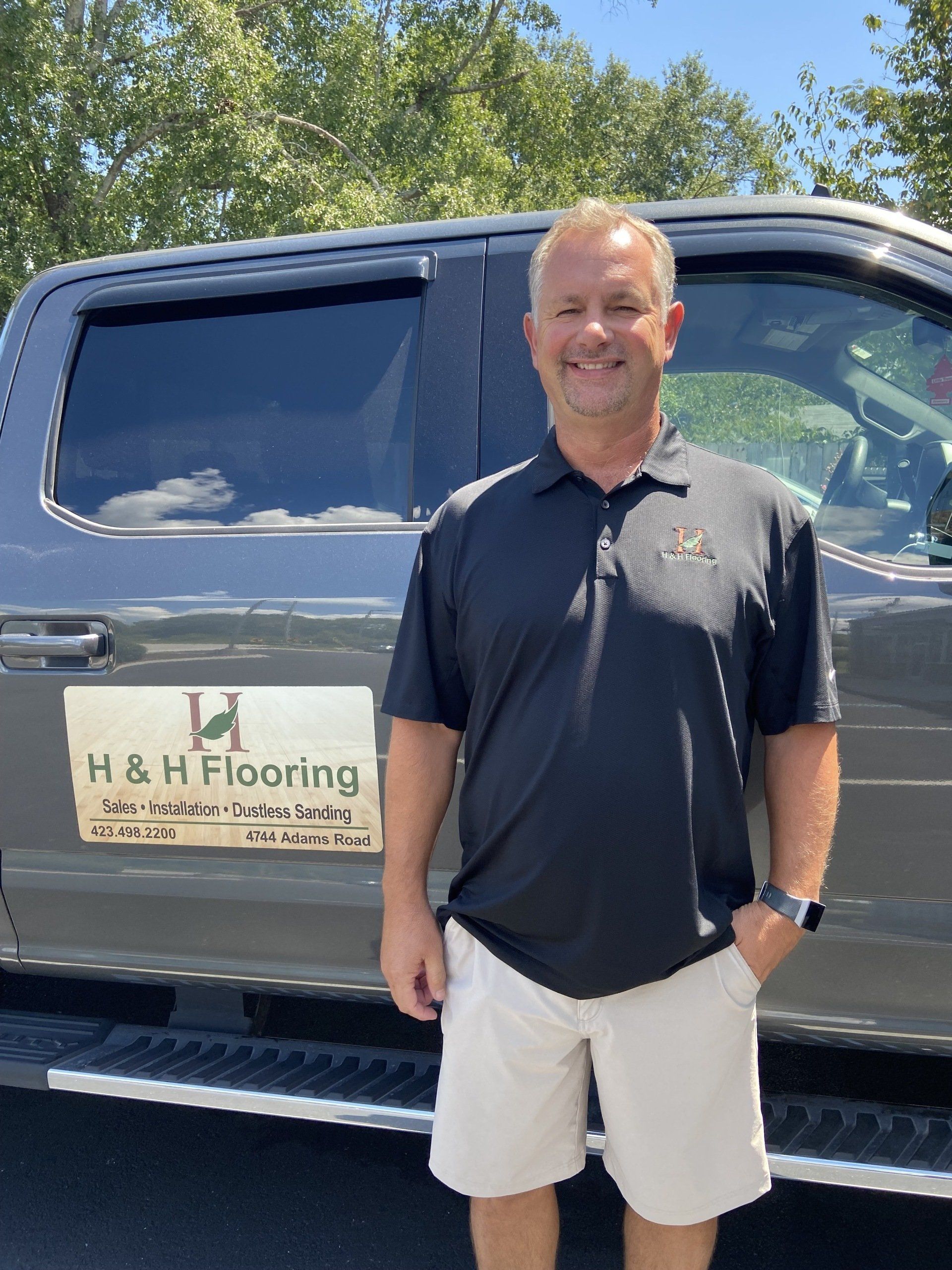 A man is standing in front of a h & h flooring truck