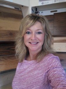 A woman in a pink shirt is smiling in front of a wooden wall.