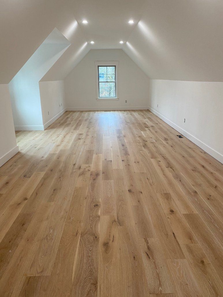 An empty attic with hardwood floors and a window.