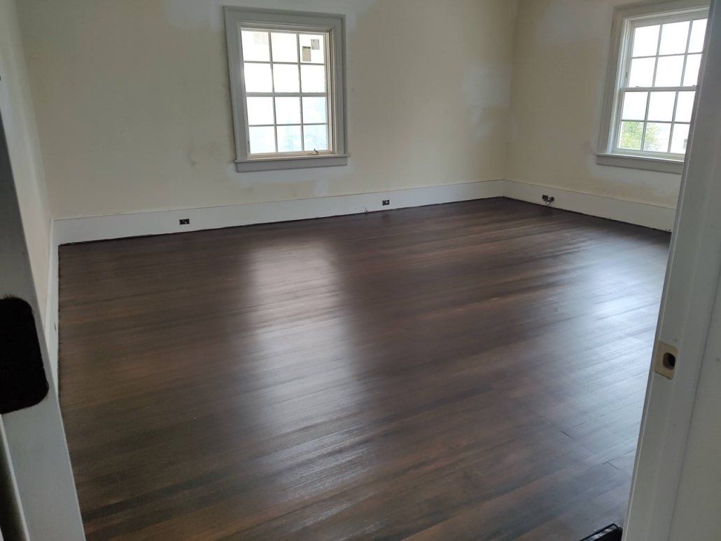 An empty room with a wooden floor and two windows.
