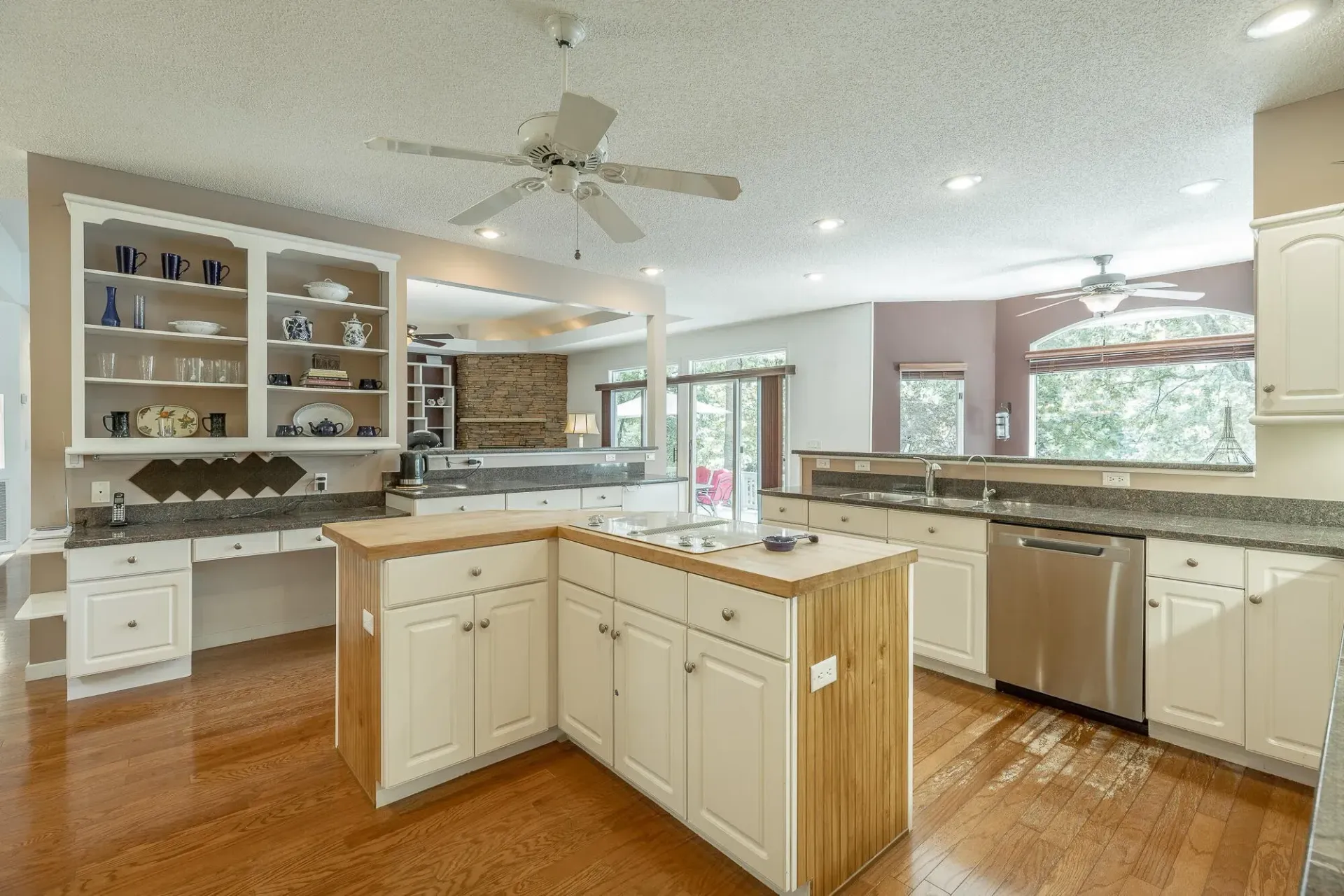 A kitchen with white cabinets , stainless steel appliances , a large island and a ceiling fan.