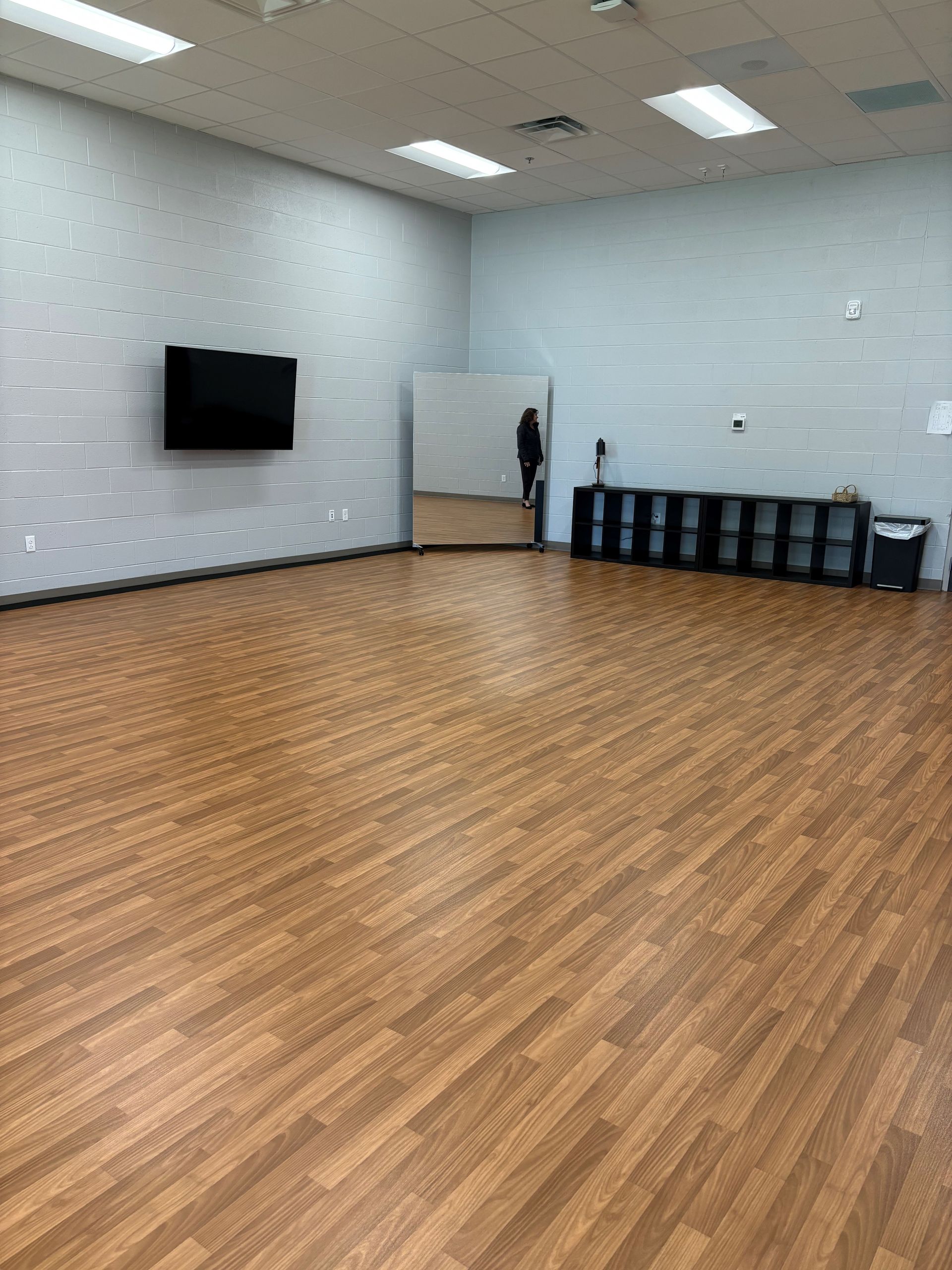 A large empty room with a wooden floor and a mirror.