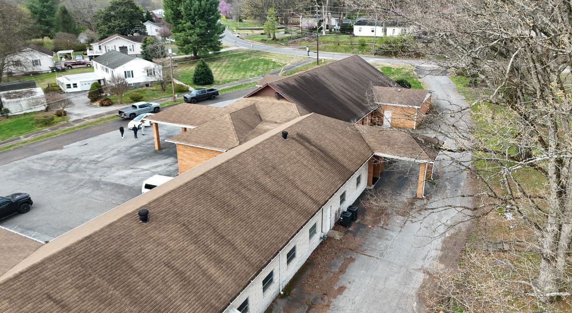 Aerial view of a low brick building with brown roof and cars parked around. People are visible.